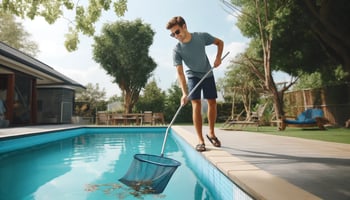 A person in navy blue maintains the pool, skimming debris on a sunny day.